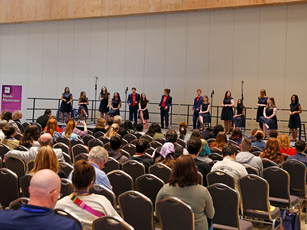 A crowd of people stand in a large open lobby watching a small group of musicians perform