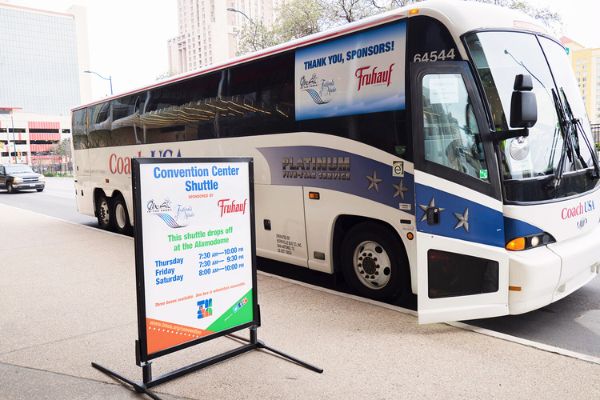 A charter bus waits near a sign displaying shuttle information